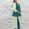 Woman wearing a sleeveless teal jacket with embroidered leaf motifs, crepe lining, and front pockets, styled over a light green kurta.